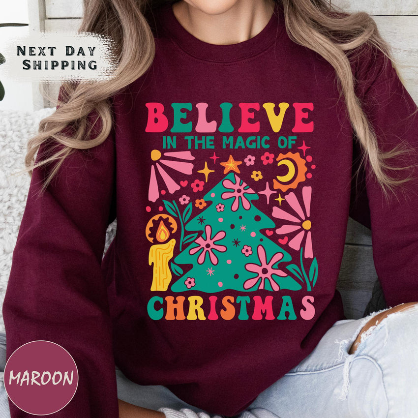 a woman wearing a maroon sweatshirt with the words believe in the magic of christmas