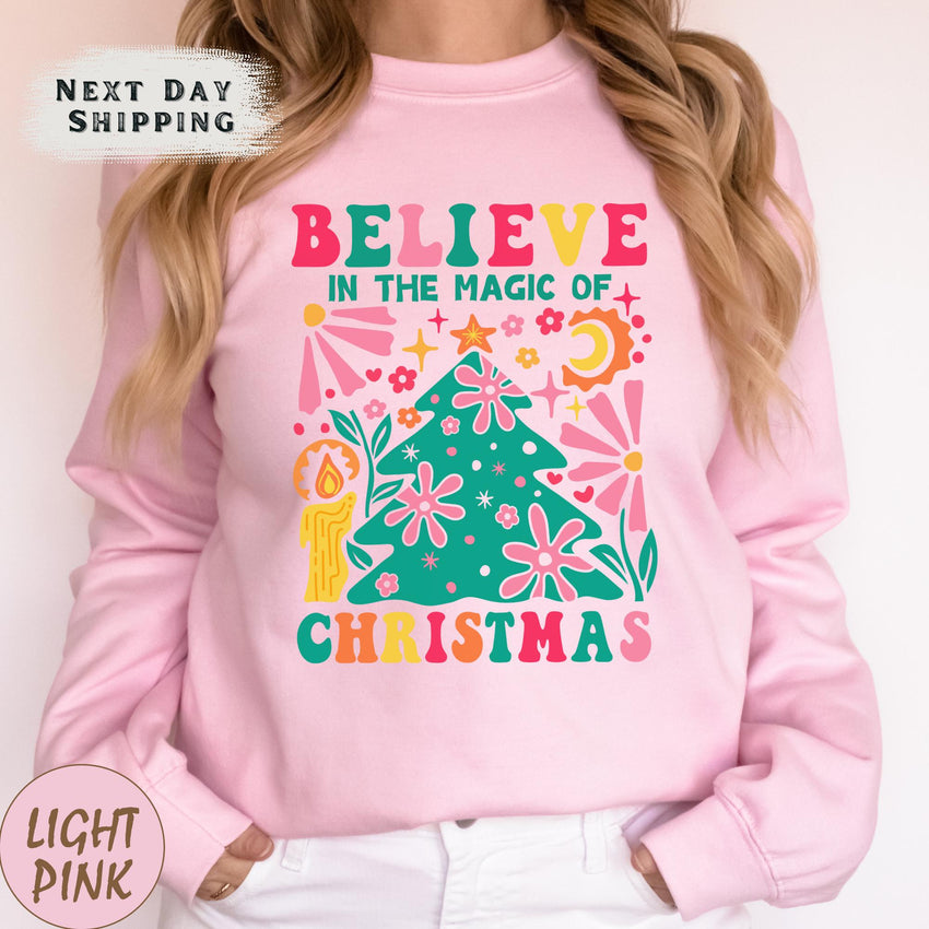 a woman wearing a pink sweatshirt that says believe in the magic of christmas