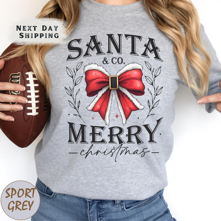 a woman holding a football and wearing a santa and merry shirt