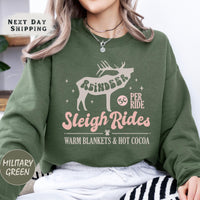 a woman wearing a green sweatshirt that says reindeer sleigh rides warm blankets and